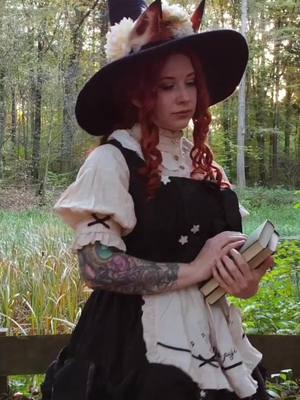 A post by @misslumina on TikTok caption: A lone witch enjoying an autumn day in the forest, surrounded by swirling leaves and earthy scents. 🍂 What mysterious potion could she be brewing in her kettle? 🖤 🦊 Fox ears: @lumitales  🧙‍♀️ Witch hat: @Costurero Real  #foxwitch #witch #witchyvibes #foxears #foxgirl #autumnwitch 