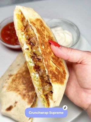 A post by @chefgenevieve on TikTok caption: Crunchwrap Supremes! Crispy, cheesy, and packed with all the good stuff. Recipe below and on my blog. This dinner recipe is quick, easy, and perfect for weeknight cravings✨ #HomemadeCrunchWrap #EasyDinnerIdeas #CrunchWrapSupremeRecipe Recipe (Serves 4) 1lb lean ground beef  1 envelope taco seasoning 3/4 cup water 5 - 10” flour tortillas (I like mission brand burrito size) 4 Tostadas  1 cup shredded Mexican blend cheese 1/2 cup sour cream 1/2 head iceberg lettuce (shredded) 2 Roma tomatoes (diced) Directions: Start by browning 1 pound of ground beef, add taco seasoning with water and cook until thickened. Shut off heat.  To a 10 inch flower tortilla, add some shredded cheese in the center followed by ground beef. Top with a tostada spread on sour cream, shredded iceberg lettuce, diced tomatoes and more cheese.  Cut another flour tortilla into quarters. Place one of the quarters on top then fold the tortilla’s sides up towards the center, folding the next piece slightly over the last.   Grill folded side down on medium low heat for two minutes, flip then grill other sude for two more minutes until golden and crispy. Slice in half and serve!  Enjoy!