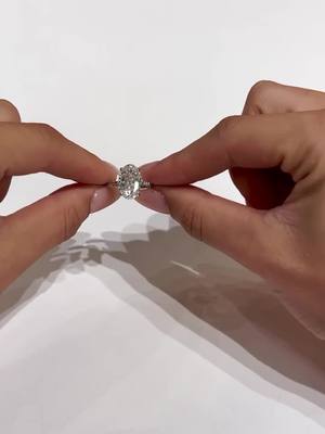 A post by @eastwestgemco on TikTok caption: One of the reasons we love our Jolie setting: the delicate tapered French pavé always looks incredibly elegant on the hand 🙌🏼 This ring is currently available! Complete with a 7.75 carat oval center, invisible halo and a donut — For $4,825 (as shown) #eastwestgemco #moissaniteengagementring #customengagmentring #eastwestjolie #7carats #ovalcut 