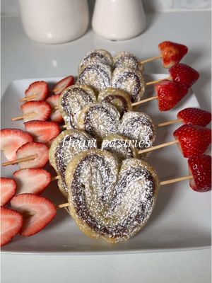 A post by @kellie_atkinson on TikTok caption: Pastry Hearts ♥️🤍 Lay out thawed puff pastry sheet Spread whatever filling you'd like, I used Nutella  Lay another sheet of pastry  Cut and shape into hearts Top with egg wash  Bake at 400 degrees for 15 minutes Top with powdered sugar Tip: Soak your skewers in water before so they don’t burn #pastry #valentine #galentinesday 