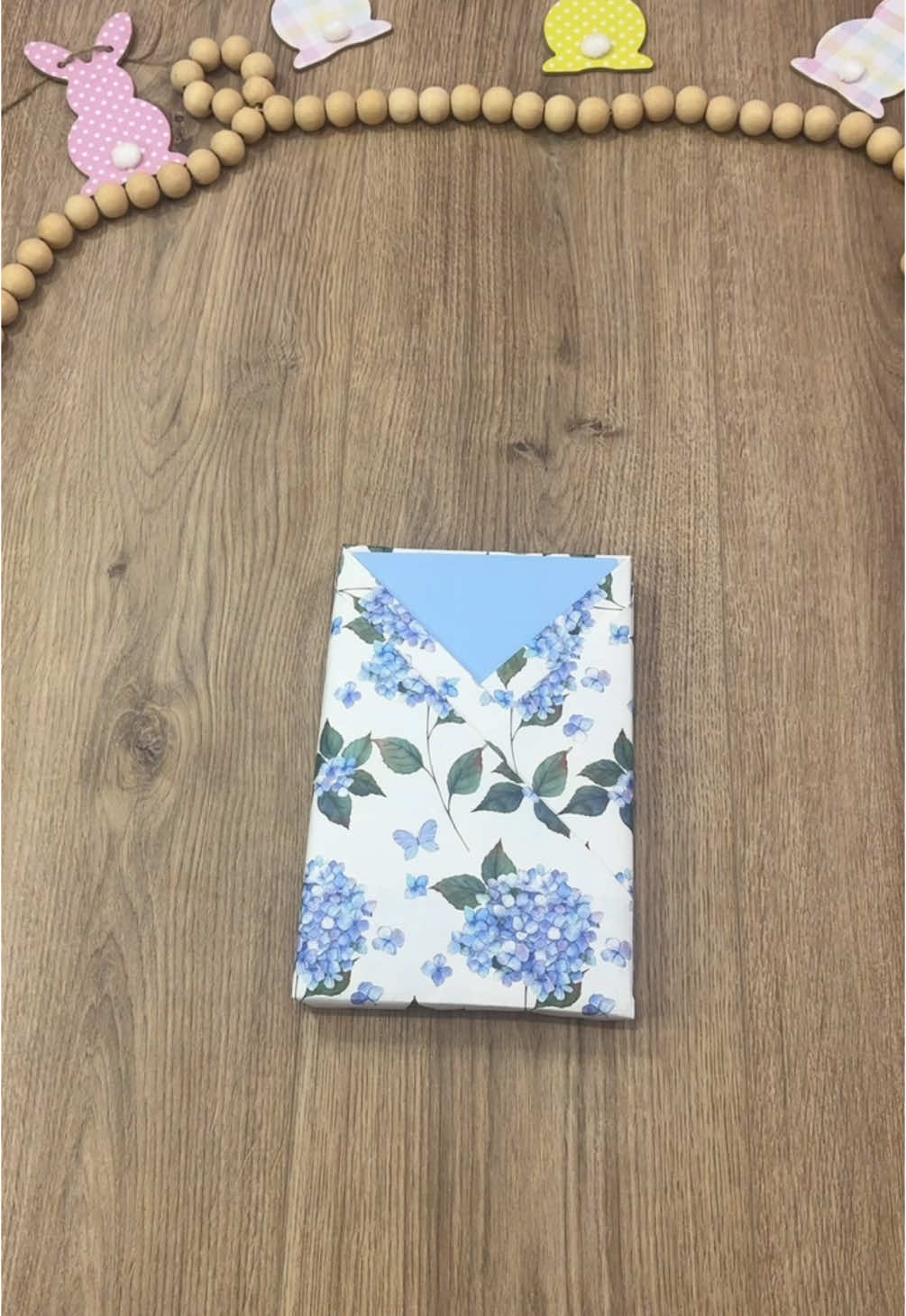 A post by @beeandblooms on TikTok caption: Another fun pocket wrap using this stunning hydrangea paper from @WRAPAHOLIC GIFT WRAPPING IDEA Loving the delicate blues and florals for a timeless touch 💙 #beeandbloomswraps #wrappinggifts #giftwrapping #wrapaholicgifts 