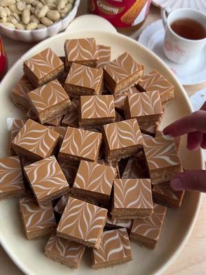A post by @kookmutsjes on TikTok caption: BISCOFF PEANUT COOKIES (NO BAKE) #food #recipe #peanut #cookies #eid #eidmubarak #nobake #biscoff #fyp #foryoupage COOKIE DOUGH 200 g Maria biscuits 165 g unsalted butter PEANUT MIXTURE 500 g unsalted peanuts 75 g sesame seeds 60 g powdered sugar 150 g biscoff spread 3 g cinnamon powder (1 teaspoon) 50 g unsalted butter FILLING 100 g biscoff spread TOPPING 125 g biscoff spread 75 g white chocolate Finely grind the Maria biscuits in a food processor. Melt 165 g butter in a saucepan over low heat. For the cookie dough, mix the melted butter with the ground biscuits. Line a springform pan with parchment paper and evenly spread the cookie dough over the base. Press firmly with the back of a spoon. Place the pan briefly in the fridge. Grind the peanuts in a food processor until smooth. Finely grind the sesame seeds in a food processor. In a bowl, combine the ground peanuts and sesame seeds. Add the powdered sugar, 150 g biscoff spread, cinnamon powder, and 50 g melted butter. Knead until smooth. Remove the springform pan from the fridge and evenly pour 100 g melted biscoff spread over the cookie base. Spread the nut mixture on top and press firmly to create a smooth surface. Melt 125 g Biscoff spread in a saucepan over low heat. Melt the white chocolate using a double boiler. Set aside 15 g and place it in a piping bag. Mix the remaining 60 g white chocolate with the melted biscoff spread until smooth. Pour the biscoff-chocolate mixture over the layer of nuts and smooth it out. Drizzle thin lines of the reserved white chocolate over the topping and create a marbled effect using a toothpick. Let the dessert set in the refrigerator for 4-5 hours, preferably overnight. Cut into squares or diamond shapes. Enjoy! Tips:   Press the base firmly with the back of a spoon or the bottom of a glass to prevent crumbling when cutting. Chill the cookie base in the fridge or freezer for 5-10 minutes for extra firmness. Lightly toast the peanuts and sesame seeds in a dry pan for enhanced flavor. When pouring the topping, quickly drizzle the white chocolate and marble it with a toothpick before it thickens. Allow the dessert to set properly before cutting. Use a sharp knife and warm it slightly under hot water for cleaner cuts. Store in an airtight container for a few days.