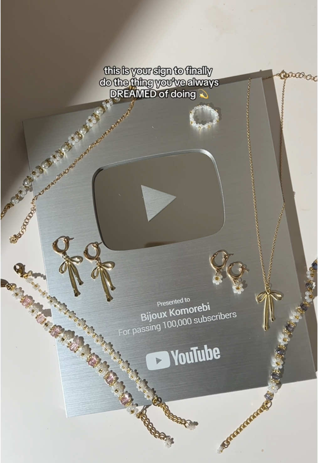 A post by @bijouxkomorebi on TikTok caption: so thankful for 100K YouTube subscribers!!! ✨ i took a chance and finally started this small jewelry business 1.5 years ago to fulfill a childhood dream and passion, and i’m filled with so much gratitude every single day for the incredible customers and community we’ve built together 🫶🏼 thank you always for your support. i hope i can continue to make your days a little brighter with my handmade pieces ✨ subscribe at the link in bio if you aren’t already for more tutorials and BTS content 💛 xo, Michelle (founder) 🫶🏼 shop my handmade pieces at bijouxkomorebi.com (link in bio) ✨ #youtubeplaybutton #youtubeplaybuttonunboxing #100ksubscribers #handmadejewelry #beadedjewelry #daintyjewelry #giftsforher #beadedbracelet #daisybracelet #SmallBusiness #beadeddaisybracelet #beadedflowerbracelet 