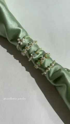 A post by @rainflower.jewelry on TikTok caption: Now available with free shipping — tap the link in my bio to order🌱✨🧚🏽 Featuring a delicate set of floral rings made with white and soft milky green beadsv💚 #floralrings #handmaderings #beadedrings #aestheticjewelry #daintyaccessories #greenandwhite #springstyle #cottagecorevibes #minimaljewelry #supporthandmade #shopsmallbusiness #trendyjewelry #fyp #viraljewelry #softaesthetic #freeworldwideshipping 