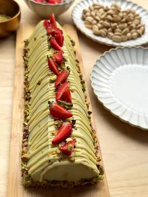 A post by @kookmutsjes on TikTok caption: PISTACHIO DESSERT (NO BAKE)     #food #recipe #pistachio #dessert #nobake #foryou #fyp CREAM 250 g mascarpone 75 g pistachio paste 35 g powdered sugar 8 g vanilla sugar (1 packet) 16 g stabilizer for whipped cream (2 packets) 400 ml heavy cream FILLING petit beurre biscuits 50 g strawberries 50 g pistachio paste GANACHE 25 ml heavy cream 60 g white chocolate TOPPING 50 g pistachios (unsalted) strawberries Place the mascarpone, pistachio paste, powdered sugar, vanilla sugar, and whipped cream stabilizer in a deep bowl. Mix for 1 minute. Gradually add the heavy cream and mix until firm. Transfer the pistachio cream to a piping bag. Lay a sheet of plastic wrap on a cutting board or tray. Arrange the petit beurre biscuits in three rows of four. Spread part of the cream over the cookies. Add another row of biscuits to the left and right sides. Pipe some pistachio paste in the center and top with pieces of strawberry. Pipe more pistachio paste on top. Spread cream all over and smooth it out evenly (save some cream for finishing). Using the plastic wrap, fold the dessert into a triangle shape by pressing the sides together. Spread the remaining cream all over the outside of the triangle. Place the dessert in the fridge and let it chill for several hours, preferably overnight, so the flavors can develop. Heat the heavy cream until just below boiling point. Add the white chocolate, let it sit briefly, then stir until smooth to create a ganache. Pipe lines of ganache over the dessert. Garnish the top with strawberry pieces and pistachios, and the base with finely chopped pistachios. Tips: Petit beurre biscuits are perfect because they don’t soften too quickly. Want a softer dessert? Dip the biscuits very briefly in milk or syrup before assembling (but don’t soak them!). Let the dessert chill thoroughly in the fridge—preferably overnight—for the best flavor and a firm shape. Use a warm knife or palette knife (dip in hot water and dry) to smooth the outside nicely.