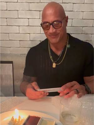 A post by @therock on TikTok caption: Opening a birthday gift - one of the most meaningful gifts I’ve ever received. A ticket 🎟️ to a wrestling show I attended when I was 11yrs old to watch my dad wrestle. Who would’ve thought years later I’d hold this ticket, and wishing I had one more shot to say hello (or goodbye) to my old man. As a kid, we were always on the road and I don’t remember my dad smiling much, as he was always mentally tired and his body banged up and in pain from the nightly grind - but he did find moments of PEACE when he was wrestling in that squared circle. Even in this video you see my dad attempting a SLIGHT SMILE 🙂 I know I’m not easy to buy gifts for, so VERY thoughtful gifts like this mean the world to me from my loved ones. Mahalo brother Brad. And my sistas Maya & Mere too. ❤️🥃 @Jon Cruz  🎞️ 🥃