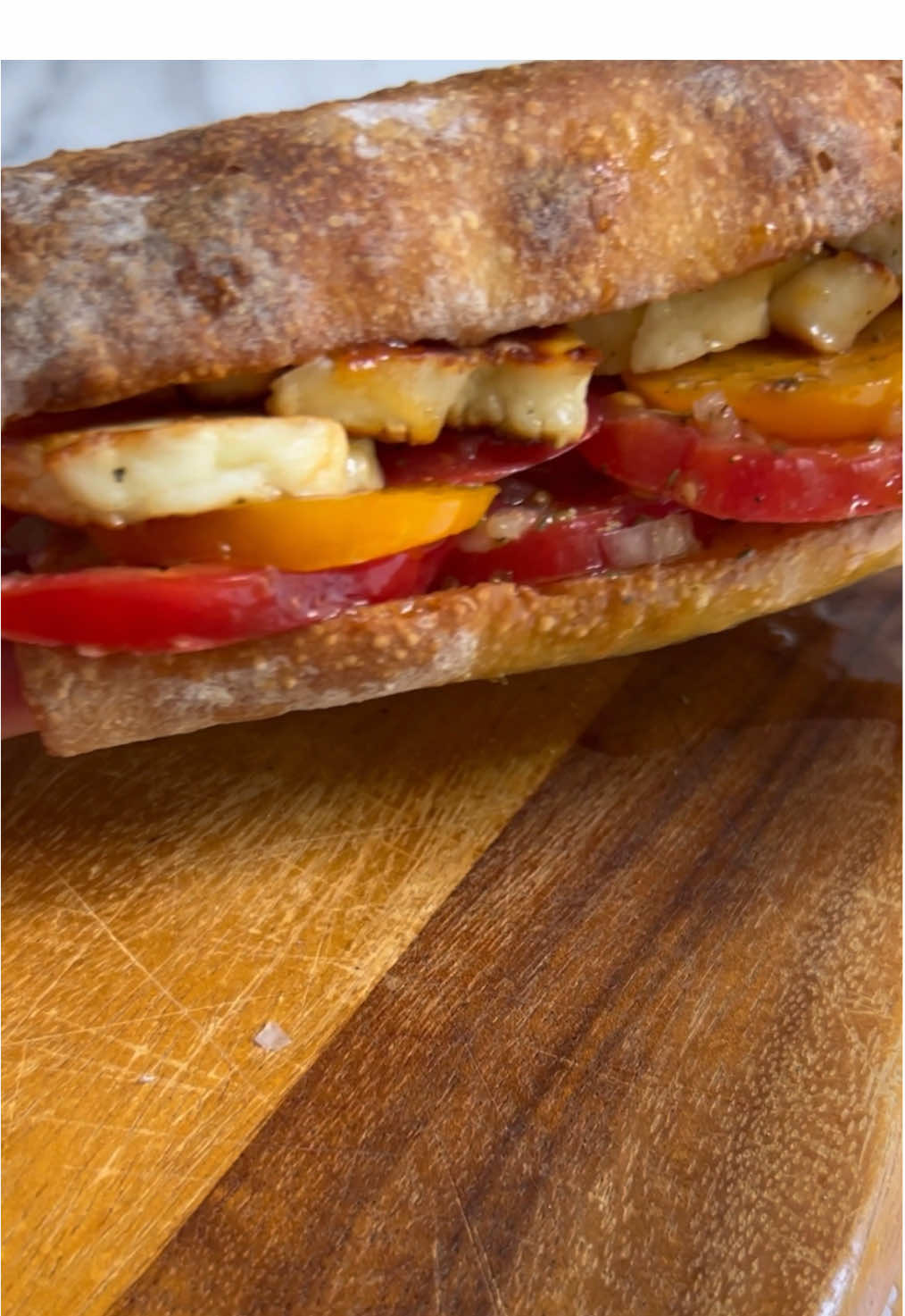 A post by @_lacebakes_ on TikTok caption: Marinated Tomato + Grilled Halloumi Sandwich Makes 2 sandwiches  2 Soft Sandwich Rolls (page 72 in my cookbook - I posted the full method in a video on 21st March!)… 1x 250g (8oz) block of halloumi cheese Olive oil for cooking the halloumi Hot honey, to drizzle. There is a recipe for hot honey on page 152 of my cookbook if you already have it!  For the tomatoes: 3 heirloom tomatoes or beef tomatoes, cut into rounds 1/4 cup (60ml) extra virgin olive oil 1.5 tablespoons (22ml) red wine vinegar 1/2 teaspoon (3g) Dijon mustard  1/2 teaspoon (3ml) honey 1/2 teaspoon flaky sea salt 1/8 teaspoons freshly cracked pepper 1 clove garlic 1 teaspoon dried oregano  1 large shallot, finely minced  Mix all the ingredients together and marinate the tomatoes for at least 15 minutes. Toast the sandwich rolls. Grill some slices of halloumi cheese in olive oil until golden on both sides and spoon some of the tomato juices over the toasted bread. Load the cheese and tomatoes onto the roll and then drizzle the sandwich with hot honey.  Enjoy! #sandwich #tomatoseason #tomatorecipes #britishsandwichweek  #foodporn #asmrcooking #asmr #sandwichrecipe #halloumi 