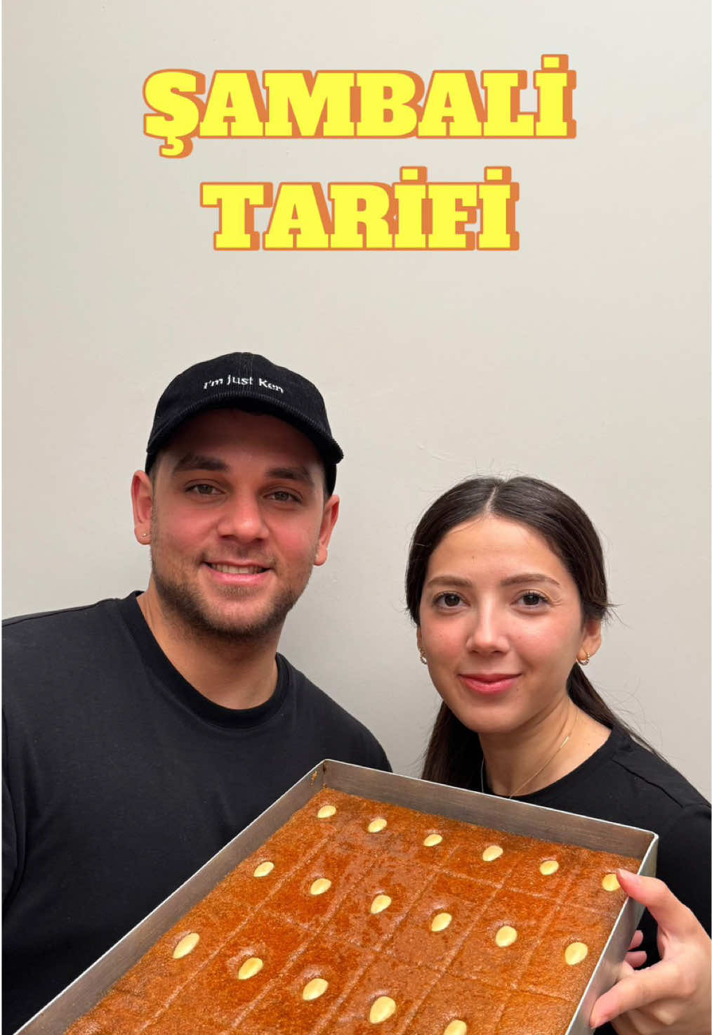 A post by @batuhanbayir on TikTok caption: Şambali Tarifi😍😋👇🏻 Bu bayram farklı bir tatlı isteyenlere;  Malzemeler 🔸5 su bardağı irmik (750gr) 🔸2 su bardağı süt(400ml süt ) 🔸1,5 su bardağı toz şeker 🔸2 paket karbonat (10gr) Şerbet 🔸5 su bardağı şeker 🔸4 su bardağı su 🔸bir kaç damla limon  🔸Çiğ badem(kabuklarını soymak için 10dk sıcak suda bekletmeniz yeterli) Tarifi  2 su bardağı ılık sütün içerisine 1,5 su bardağı toz şeker ekliyoruz. Şeker sütün içerisinde eriyinceye kadar güzelce karıştırıyoruz. Diğer taraftan yoğurma kabına 5 su bardağı irmik, 1 tatlı kaşığı dolusu karbonatı ekliyoruz.Ilıttığımız sütü irmiğin üzerine yavaş yavaş boşaltıp ve tüm malzemeyi  tahta kaşık yardımı ile karıştırıyoruz. Tüm harcı güzelce karıştırdıktan sonra kabın üzerini streç filmle kapatarak 12 saat dinlenmesi için buzdolabına kaldırıyoruz.Yeterince dinlendirdiğimiz irmiği dolaptan çıkardıktan sonra bi 15-20 dakika bekletip ardından elimizde irmiği 3-4 dakika kadar yoğuruyoruz. Daha sonra tabanını yağladığımız fırın tepsisinin içerisine hamuru boşaltalım. Ben 25x35 santimetrelik baklava tepsisi kullandım. Hamuru tepsiye eşit miktarda dağıttıktan sonra üzerini önce elimizle daha sonra bir spatula yardımıyla güzelce düzeltiyoruz. Eşit boyutta olmasına dikkat ederek tatlımızın üzerine dikdörtgen izler oluşturuyoruz dibine kadar kesmiyoruz.  Bademleri yerleştirip 180derece fırında 35 dakika fansız fırına gönderiyoruz. Şerbetini hazırlayıp kaynamaya başladıktan sonra 10-15 dakika kısık kaynatmaya devam ediyoruz.dilerseniz bir kaç damla limon sıkabilirsiniz. En son sıcak tatlıya sıcak şerbeti döküyoruz burası önemli ikisi de sıcak olacak. Ardından çekmesini bekliyoruz. Tüm şerbetini çekip soğuduktan sonra 4-5 saat bu şekilde dinlendirelim. Tarifimiz hazır. Afiyet olsun :) #batuhanbayır #şambali @Ayyüce kamit 