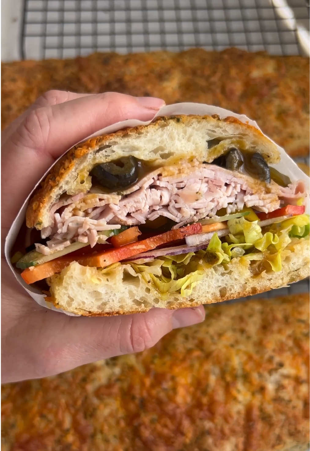A post by @_lacebakes_ on TikTok caption: FOOTLONG SANDWICH TIME! Italian Herb & Cheese Sandwich Roll method was shared a couple of posts back if you’d like to see it with a voiceover explaining all the steps! Ingredients: 1x batch same-day focaccia dough (recipe is pinned at the top of my page here or page 22 in my cookbook) Extra virgin olive oil 1 Tablespoon dried oregano 1 Tablespoon dried parsley 1.5 Tablespoons dried garlic granules 4 Tablespoons grated Parmesan cheese ½ cup (50g) grated cheese (I used a blend of white cheddar, Monterey Jack and Red Leicester…just use whatever you have on hand).  Follow my recipe for same-day focaccia. Prepare a large baking tray (half sheet pan or approx 18x13 inches) with nonstick parchment and 2-3 tablespoons of extra virgin olive oil.  When it’s finished proofing in the bowl, tip the dough onto the tray and fold it into thirds as instructed in the focaccia recipe and then flip it over. Cover and proof for another 1-1.5 hours.  Mix together the oregano, parsley, garlic granules and grated Parmesan cheese. Preheat the oven to 220C/430F with the shelf set to the lowest position.  Drizzle the dough with extra virgin olive oil. Sprinkle ¾ of the herb mixture evenly over the top of the dough and then dimple it in. Do not spread the dough all the way to the edges of the tray (the rolls would be too thin). There should be some empty tray bordering the dough (use the tutorial for visual guidance). Oil a sharp bench scraper or knife and cut the dough into 4 footlong sandwich rolls (make as even as possible). Oil the scraper between cuts so the dough doesn’t stick. You may need to use your hands to help separate the cuts (as I do in the video). Spread the rolls evenly apart from each other, sprinkle over the grated cheese and the remaining herb mixture and then gently pat into the dough. Bake on the bottom rack for 18-20 minutes or until the cheese is toasted and the rolls are a light golden brown. Transfer to a cooling rack and after ten minutes, enjoy!  #sandwich #subway #bread #breadmaking #copycatrecipe