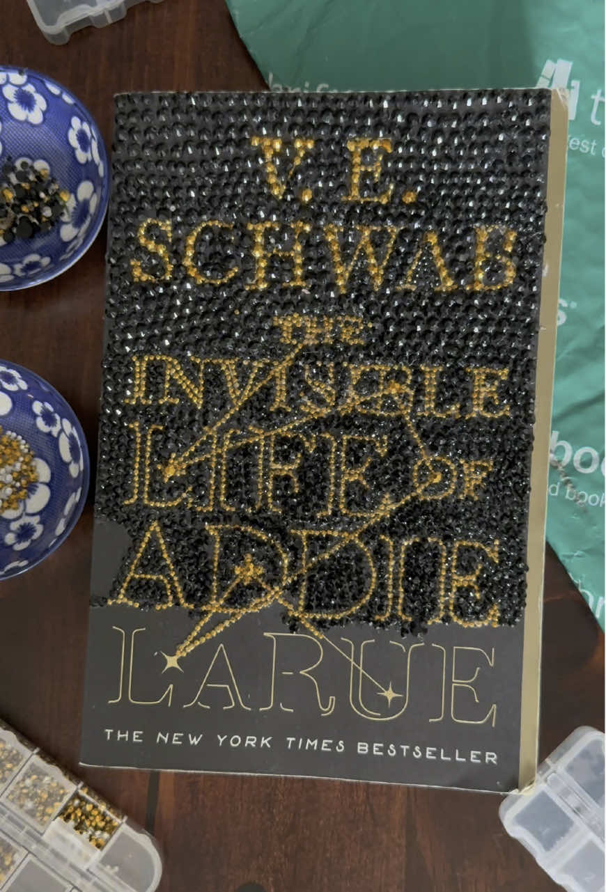 A post by @thriftbooks on TikTok caption: One of the most anticipated books of the year is dropping tomorrow and we came prepared. A member of our social media team bedazzled her favorite V.E. Schwab book (The Invisible Life of Addie LaRue) in preparation to present it to her at the LA Times Festival of Books. Tell us if you’re ready for V.E. Schwab’s latest, Bury Our Bones In The Midnight Soil. #thriftbooks #readersgonnaread #readerlife #BookTok #veschwab #bookbedazzle #theinvisiblelifeofaddielarue #buryourbonesinthemidnightsoil 