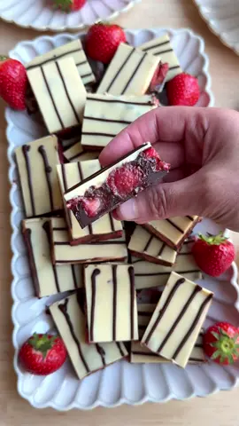 A post by @kookmutsjes on TikTok caption: STRAWBERRY CHOCOLATE BARS #food #recipe #foryou #fyp #chocolate #strawberries #bars #dessert BASE 150 g milk chocolate FILLING 150 g dark chocolate 100 ml heavy cream 400 g strawberries TOPPING 175 g white chocolate 25 g dark chocolate Melt the milk chocolate (150 g) using a bain-marie (double boiler). Heat the heavy cream (100 ml) in a small saucepan until it’s almost boiling. Remove from the heat and add the dark chocolate (150 g) in pieces. Let sit for 1 minute, then stir until smooth. Cut the strawberries (400 g) into pieces and place them in a bowl. Add the chocolate ganache and mix until well combined. Pour the melted milk chocolate into a baking dish and spread it evenly over the base. Spread the strawberry mixture evenly on top. Place in the refrigerator and let it set completely (at least 1 hour). Melt the white chocolate (175 g) using a bain-marie. Pour the melted white chocolate over the chilled filling. Melt the dark chocolate (25 g) using a bain-marie and pour into a piping bag. Pipe thin lines over the white chocolate. Freeze for at least 1–2 hours to fully set. Cut into pieces and serve.