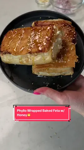 A post by @arielwinter on TikTok caption: Guys… feta is one of my favorite foods ever so if you feel the same this simple recipe is GIVING and you have to try!!! Recipe inspired by @The Mediterranean Dish ✨ 2 blocks of feta— 4oz each  Phyllo dough, thawed Honey Sesame Seeds Preheat your oven to 350 degrees. Unwrap your phyllo dough and spread it carefully on a clean surface or cutting board. Brush the surface of the phyllo dough with olive oil, then add one of the feta blocks to the phyllo towards the bottom closest to you. Fold the sides to almost cover the cheese. Then brush the phyllo with olive oil again. Continue to fold the phyllo around the feta until completely folded. Repeat with the 2nd block of feta and remaining phyllo dough sheets. Brush the top of both wrapped phyllo blocks with more olive oil and then arrange them seam side down on a nonstick baking sheet. Bake them in the oven for about 20 minutes, until the phyllo is golden and crispy on both sides. Once it’s done, remove it from the oven very carefully and transfer to the serving plate! Drizzle with honey and sprinkle with sesame seeds. Serve and enjoy!!!!! PS. I used too much feta and it came out the sides so use only 4oz instead of a whole block for each!  #feta #greekrecipes #bakedfeta 