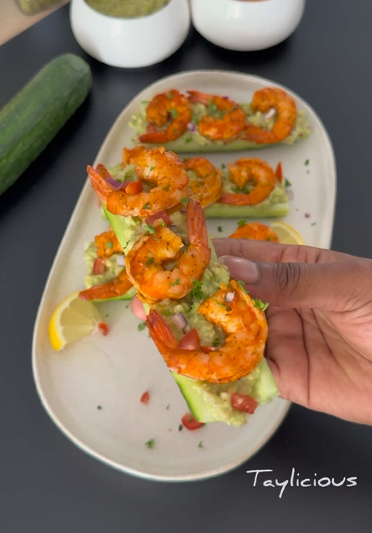 A post by @tay_liicious on TikTok caption: Concombres Farcis Avocat & Crevettes 🥒🦐   Ingrédients : 1 grand concombre 🥒  2 avocats bien mûrs 🥑 Une douzaine de crevettes 🦐 1/2 oignon rouge 🧅 Jus de citron 🍋  Épices: piment de Cayenne, épice Plein Sud, paprika fumé, Persillade, Poivre, Sel aromatisé, Persil frais, citron  1. Dans une poêle, fais revenir les crevettes dans un petit morceau de beurre. Assaisonne avec de la persillade, du poivre, du paprika fumé et l’épice Plein Sud. Une fois bien dorées, réserve les 2. Épluche le concombre, coupe le en deux, puis encore en deux dans la longueur. Retire les extrémités et évide l’intérieur à l’aide d’une cuillère 3. Écrase deux avocats dans un bol. Ajoute l’oignon rouge finement haché, du jus de citron, de l’huile d’olive et les épices notées plus haut. Mélange bien le tout jusqu’à obtention d’une texture crémeuse 4. Remplis les barquettes de concombre avec une belle couche de guacamole. Dispose ensuite les crevettes par-dessus 5. Saupoudre de persil frais et de petits dés de tomate et c’est prêt 😍 #concombre #concombrefarcie #guaccamole #avocat #crevette #recette #ete #recetterapide #recettefacile #tayliicious 