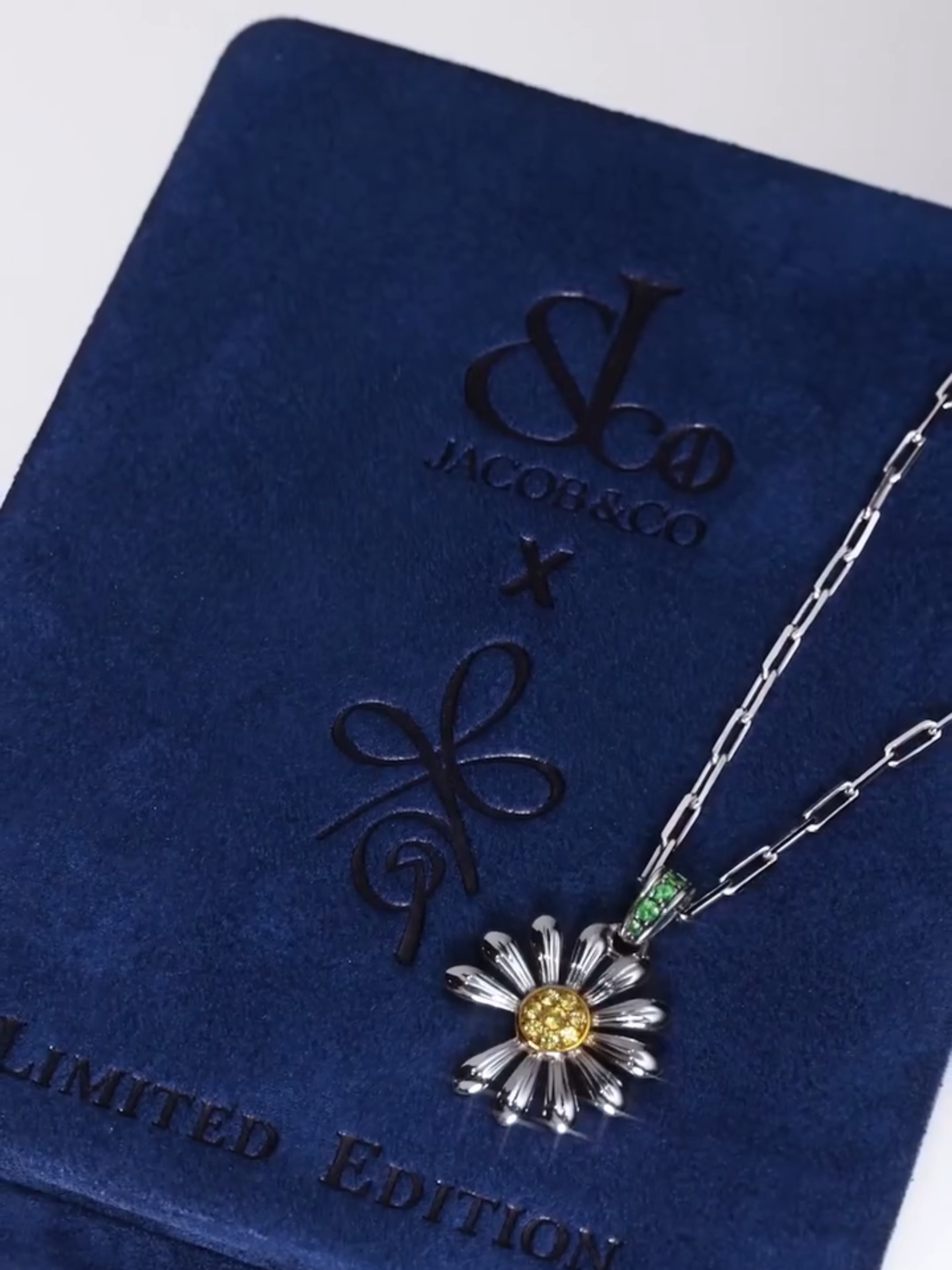 A post by @jacobandco on TikTok caption: "Why is one petal always missing?" G-Dragon’s daisy isn’t a flaw — it’s a philosophy. A symbol of contrast, imperfection, and identity. Now reimagined as a fine jewelry pendant. #PEACEMINUSONE #JacobAndCo #GDRAGON #InspiredByTheImpossible