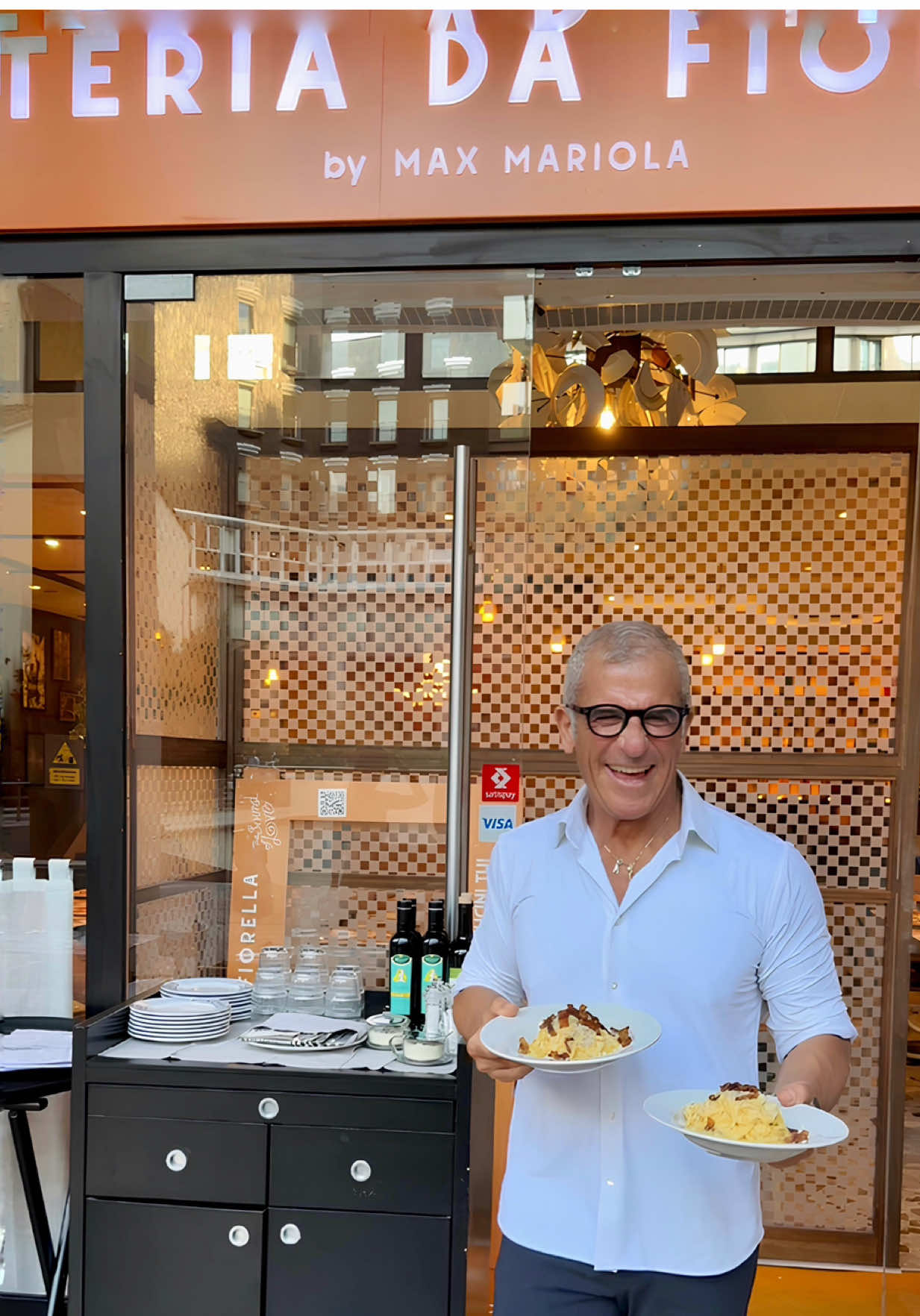 A post by @chefmaxmariola on TikTok caption: Ci avete travolto. Letteralmente. 💥 Dovevamo riprenderci un attimo dall’emozione, ma non ci siamo dimenticati di voi ❤️ 📍L’apertura  della nuova 𝗢𝘀𝘁𝗲𝗿𝗶𝗮 𝗱𝗮 𝗙𝗶𝗼𝗿𝗲𝗹𝗹𝗮 a 𝗠𝗶𝗹𝗮𝗻𝗼, in 𝗟𝗮𝗿𝗴𝗼 𝗖𝗼𝗿𝘀𝗶𝗮 𝗱𝗲𝗶 𝗦𝗲𝗿𝘃𝗶 𝟭𝟭, è stata una giornata che non dimenticheremo. Ci avete riempito il cuore… e tutto questo è stato possibile grazie a voi. 💥 𝗗𝗮 𝗼𝗴𝗴𝗶 𝗽𝗼𝘁𝗲𝘁𝗲 𝗮𝗻𝗰𝗵𝗲 𝗽𝗿𝗲𝗻𝗼𝘁𝗮𝗿𝗲 𝗶𝗹 𝘃𝗼𝘀𝘁𝗿𝗼 𝘁𝗮𝘃𝗼𝗹𝗼! Vi aspettiamo nel cuore di Milano, a due minuti dal Duomo, con la cucina romana più vera che c’è. 👉 Qual è il piatto romano che volete assolutamente trovare nel menù? Scrivetecelo nei commenti 👇 #osteriadafiorella #maxmariola #thesoundoflove #maxmariolacucinapervoi