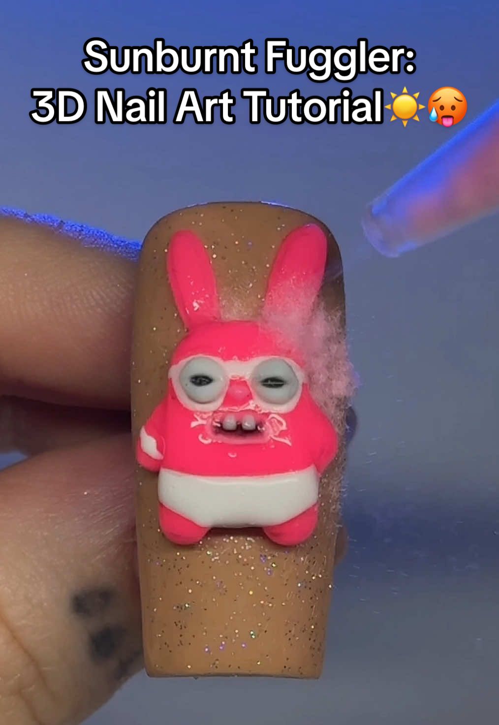 A post by @nailzbydevshop on TikTok caption: This Fuggler has had enough of summer!☀️🤣 Who else has gotten a sunburn this year already?🙋‍♀️😭 We used our NAILZBYDEV products to create this little cutie, including our "What The Fluff?" sprayable fluff to give him those extra plushie vibez!🩷🔥 Who's going to try this fun tutorial out?😍👏 #nails #nailart #nailtutorial #fugglers #nailzbydevshop #3dnailart #gelnails #whatthefluff #fluffynails #nailsoftiktok 