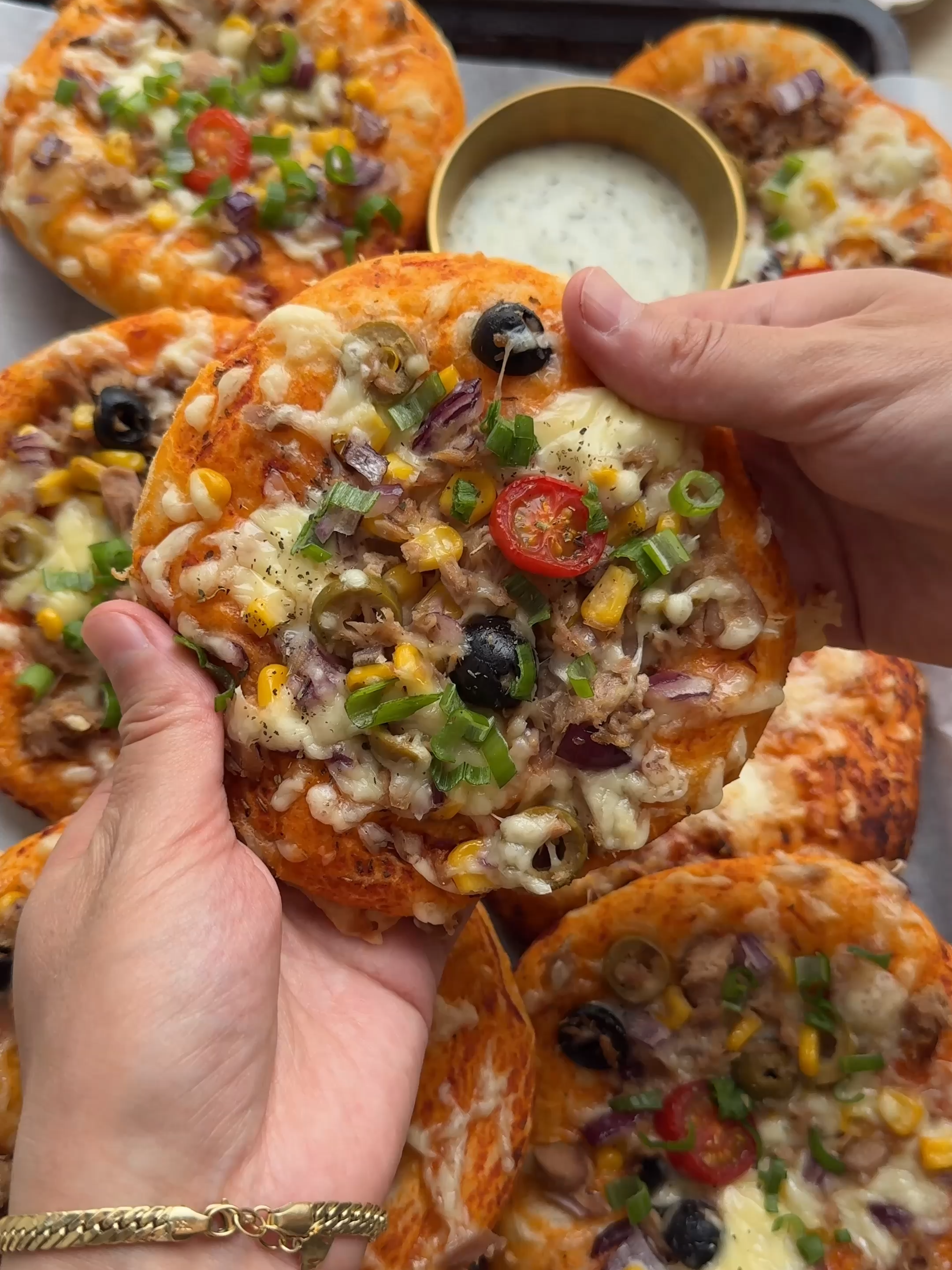 A post by @kookmutsjes on TikTok caption: SOFT MINI PIZZA’S WITH TUNA #food #recipe #pizza #tuna #fish #cheese #tasty #fy #fyp #foryoupage   DOUGH 160 ml lukewarm water 7 g instant yeast 12 g honey 35 ml sunflower oil 75 g yogurt 450 g flour (all-purpose or patent flour) 8 g salt (1⅓ teaspoons) EXTRA fine semolina TOMATO SAUCE 100 ml water 70 g tomato paste 2 g oregano FILLING cheese slices (young cheese) TUNA MIXTURE 140 g tuna (in sunflower oil) 50 g red onion (half a red onion) 50 g corn 40 g green olives 30 g black olives TOPPINGS grated cheese cherry tomatoes cheese spread Instructions: Add the lukewarm water, yeast, and honey to a deep bowl. Mix well and let it rest for 5 minutes. Add the sunflower oil and yogurt. Mix until combined. Add the flour and salt. Knead for 10–12 minutes until smooth. Cover and let the dough rise for 1 hour, or until doubled in size. Meanwhile, mix the tuna with finely chopped red onion, corn, and sliced green and black olives in a bowl. Set aside. Mix the tomato paste, water, and oregano until smooth. After rising, deflate the dough and divide it into 9 equal pieces, about 75 grams each. Shape into balls. Take one ball and roll it out into a flat circle. Spoon some tomato sauce into the center and place a slice of cheese on top. Fold the edges toward the center and pinch to seal. Sprinkle some fine semolina on a plate and roll the filled dough through it. Place it on your work surface and gently roll it flat. Place the dough on a baking tray lined with parchment paper. Brush with tomato paste, sprinkle grated cheese over it, and top with the tuna mixture. Optionally, add a slice of cherry tomato and a bit of cheese spread. Let the mini pizzas rise for 30 minutes. Bake the pizzas in a preheated oven at 220 °C (428°F top and bottom heat) for 12–18 minutes, until golden brown.