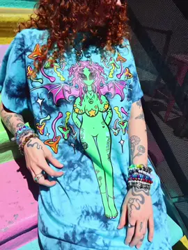 A post by @trippydraws on TikTok caption: NEW shirts, tapestrys, sticker packs,back packs, ALL ON MY SHOP JULY 5TH AT 5PM ❤️🪐🪿🎨✨🌈🌀 my biggest drop ive ever done!❤️❤️❤️❤️ #tiktok #ravewear #ravers #musicfestival 