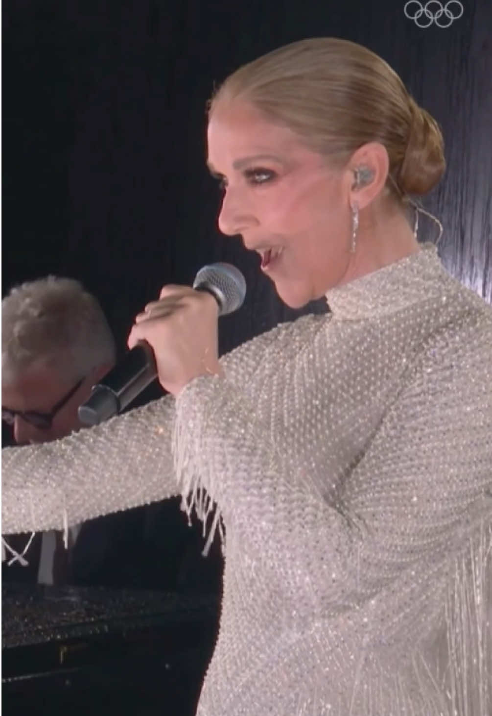 A post by @olympics on TikTok caption: One year ago today, Celine Dion lit up the stage at the #Paris2024 Opening Ceremony. 🎤  A breathtaking performance we're still not over! 🇫🇷✨ #Olympics 